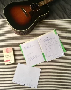 feuilles lignés, dictionnaire de rimes et guitare lors d'une séance de rédaction poétique.